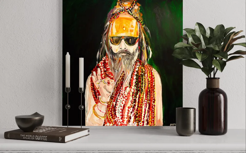 Yana Yank's portrait of a sadhu with beads and a saffron turban displayed on a shelf beside candles and a plant